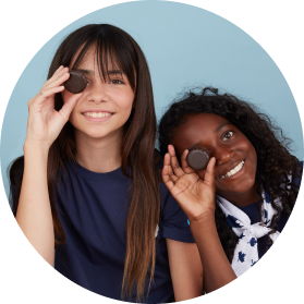 Two girls smiling and holding Girl Guide cookies up to their eyes like playful monocles.