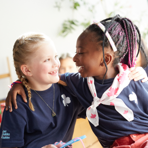 Two girls smiling at each other with their arms around one another