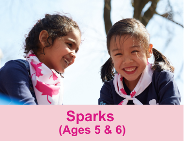 Young girls in Girl Guides uniforms smiling and laughing outdoors.