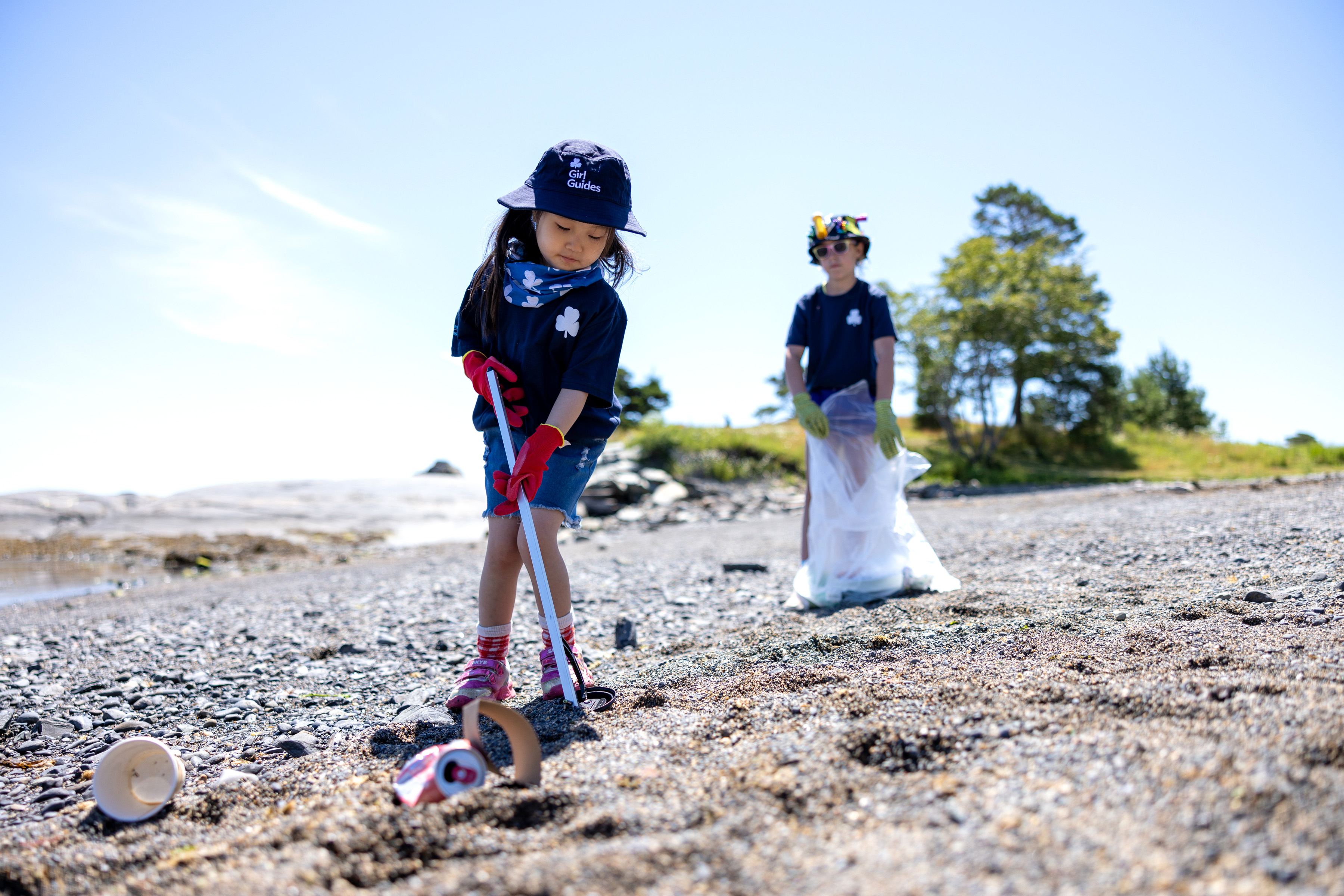 Two young girls cleaning up trash on a beach. 